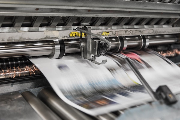 A printing press runs a sheet of paper through it